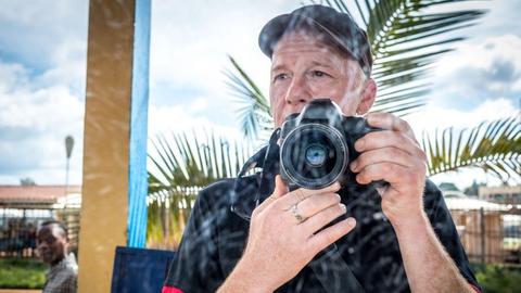 Selbstportrait des Fotografen Karsten Thielker - Spiegelung in einer Fensterscheibe. Im Hintergrund Palmen und eine weitere Person.