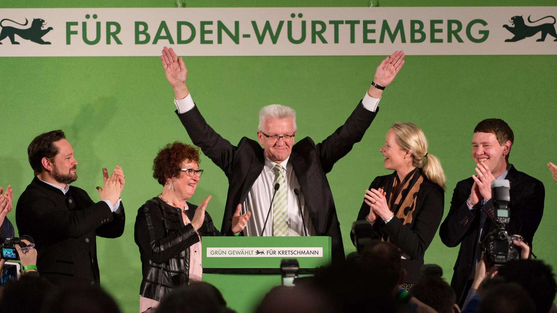 Winfried Kretschmann und seine Frau Gerlinde stehen auf einem Podium und lassen sich feiern, Kretschmann streckt die Arme in die Luft.