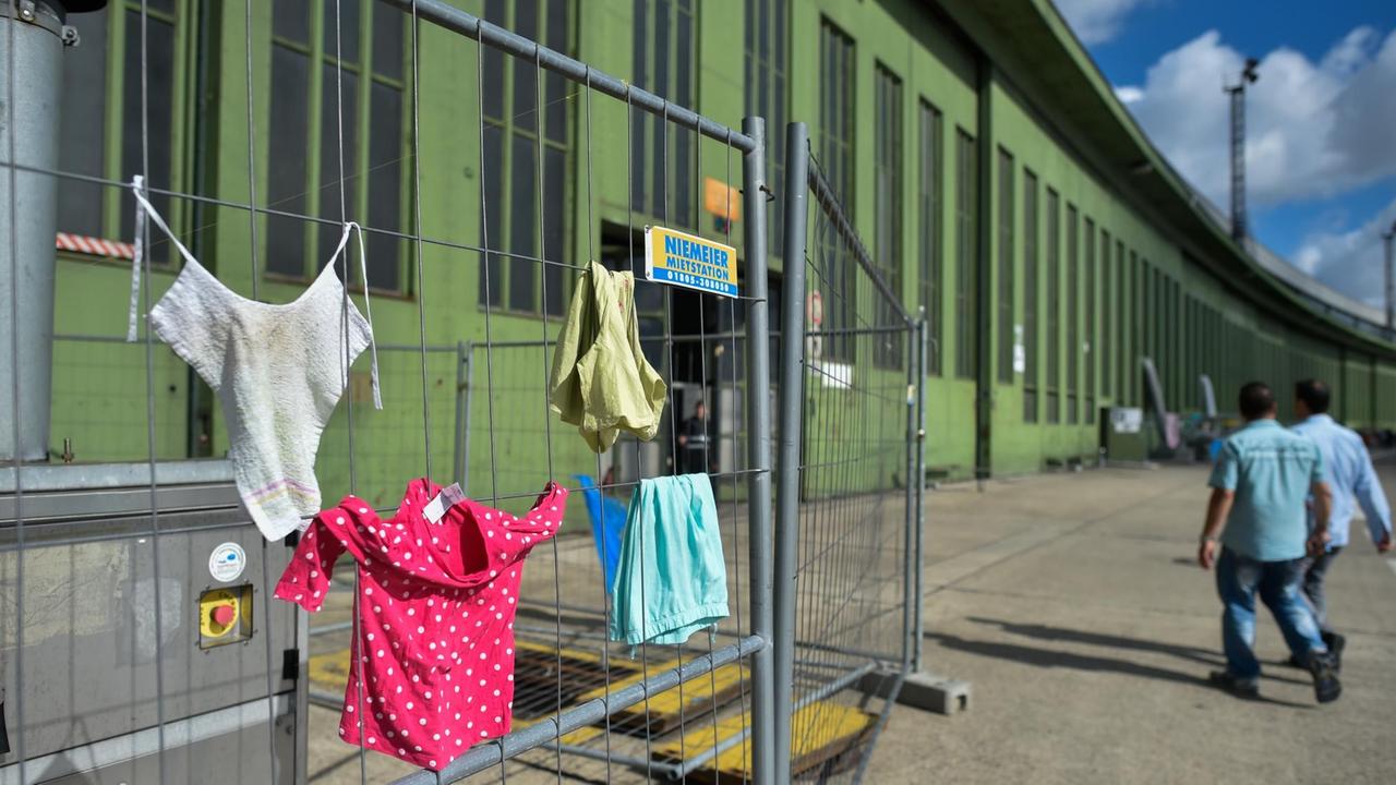 Kinderkleidung hängt am 07.07.2016 in Berlin vor einem Hangar der Flüchtlingsunterkunft auf dem Gelände des ehemaligen Flughafens Tempelhof an einem Bauzaun zum trocken in der Sonne.