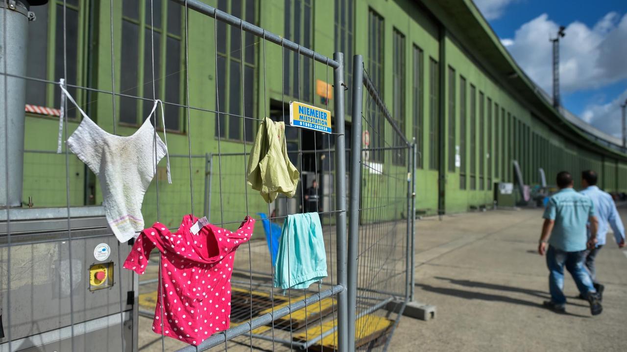 Kinderkleidung hängt am 07.07.2016 in Berlin vor einem Hangar der Flüchtlingsunterkunft auf dem Gelände des ehemaligen Flughafens Tempelhof an einem Bauzaun zum trocken in der Sonne. Kinderkleidung hängt am 07.07.2016 in Berlin vor einem Hangar der Flüchtlingsunterkunft auf dem Gelände des ehemaligen Flughafens Tempelhof an einem Bauzaun zum trocken in der Sonne.