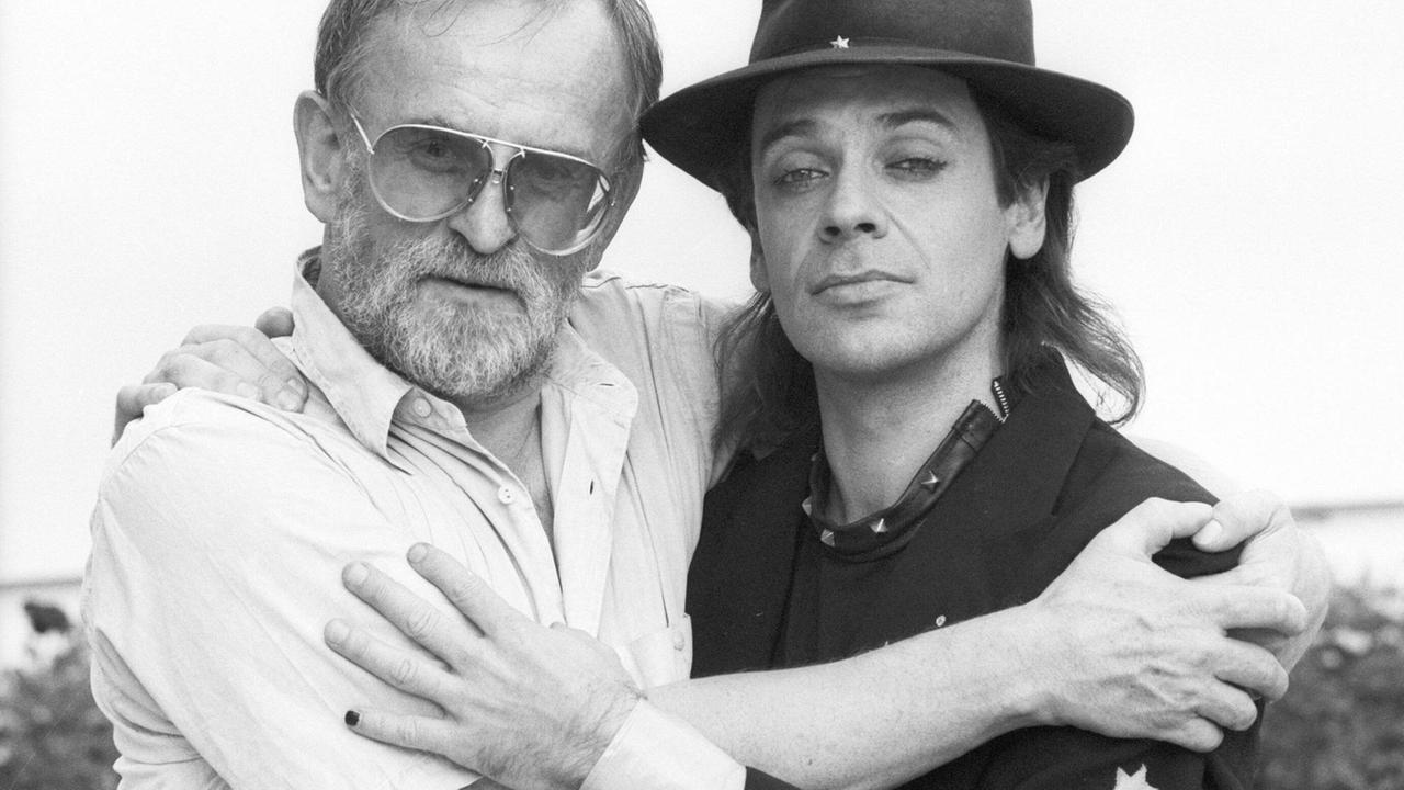 Fritz Rau und Udo Lindenberg umarmen einander und blicken in die Kamera. Rau trägt weiß, Lindenberg schwarz. Fritz Rau und Udo Lindenberg umarmen einander und blicken in die Kamera. Rau trägt weiß, Lindenberg schwarz.