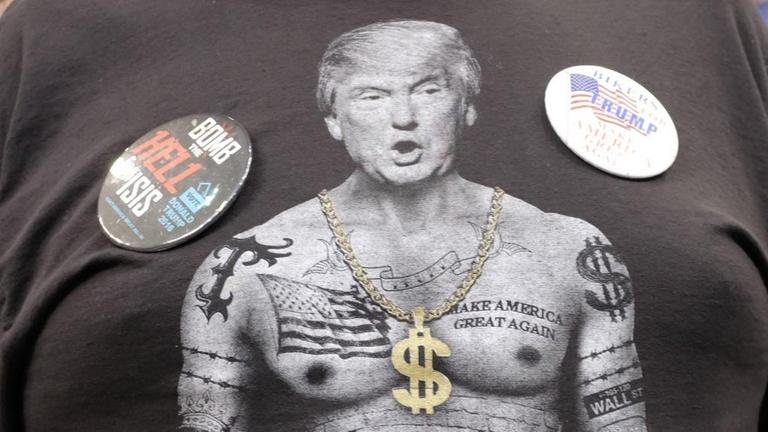 Ein Unterstützer des US-Präsidenten Donald J. Trump trägt ein T-Shirt mit eine Monage aus Donald Trum und einem muskulösen Rapper mit Goldkette und anderen Insignien.