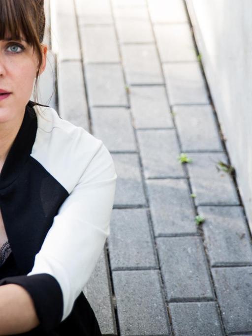 Sarah Kuttner sitzt auf einer Treppe und schaut in die Kamera.