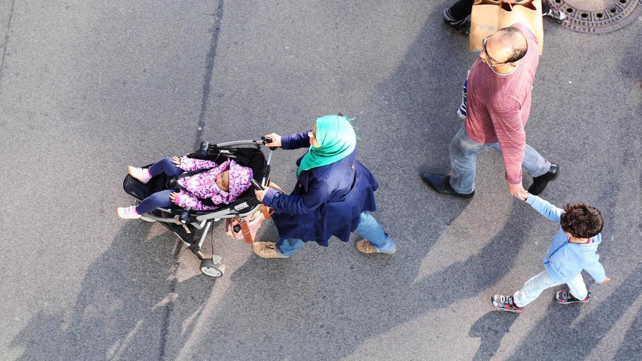 Eine junge muslimische Familie geht im Stadteil Steglitz in Berlin über einen Fußweg an einer Einkaufsstraße. Die Frau trägt ein Kopftuch und schiebt ein Kleinkind im Kinderwagen. Der Mann hält einen kleinen Jungen an der Hand. Eine junge muslimische Familie geht im Stadteil Steglitz in Berlin über einen Fußweg an einer Einkaufsstraße. Die Frau trägt ein Kopftuch und schiebt ein Kleinkind im Kinderwagen. Der Mann hält einen kleinen Jungen an der Hand.