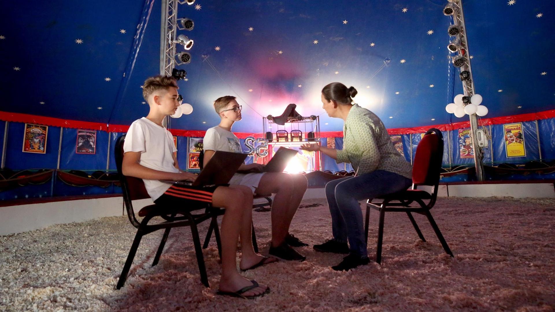 Die beiden Circuskinder Toni (l) und Jami sitzen mit einer Lehrerin in der Manege eines Zirkuszeltes. Die beiden Circuskinder Toni (l) und Jami sitzen mit einer Lehrerin in der Manege eines Zirkuszeltes.