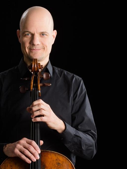 Der Cellist hält sein Instrument vor sich und stützt sein Kinn darauf.