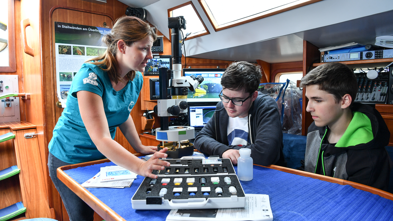 Die wissenschaftliche Mitarbeiterin Elisa Czech (l.) weist die beiden Schüler Philipp und Silas (r.) auf dem Forschungsschiff "Aldebaran" im Hafen von Konstanz in die Arbeit mit einem Mikroskop an Bord ein. Die wissenschaftliche Mitarbeiterin Elisa Czech (l.) weist die beiden Schüler Philipp und Silas (r.) auf dem Forschungsschiff "Aldebaran" im Hafen von Konstanz in die Arbeit mit einem Mikroskop an Bord ein.
