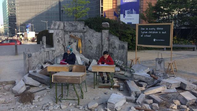 Zwei Kinder sitzen vor einer Bauruine an einem Schreibtisch