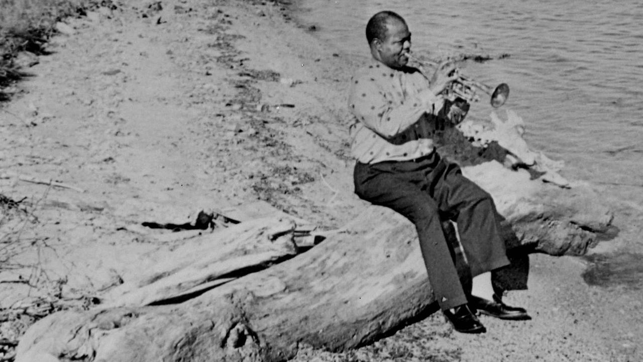 Der Jazztrompete Louis Armstrong sitzt auf einem Baumstamm am Meeresstrand, auf dem er einsam sitzt und spielt. Der Jazztrompete Louis Armstrong sitzt auf einem Baumstamm am Meeresstrand, auf dem er einsam sitzt und spielt.
