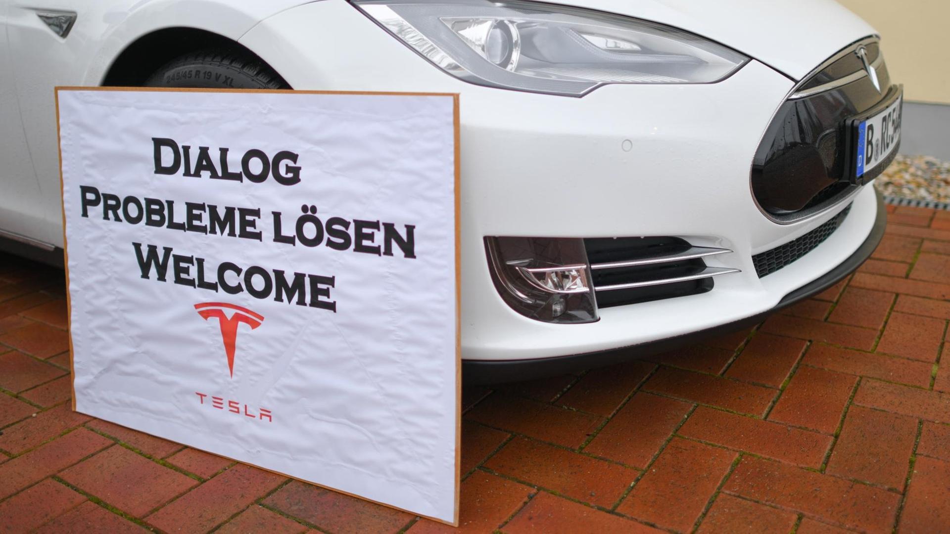 Ein Schild mit der Aufschrift "Dialog Probleme Lösen Welcome Tesla" steht an einem Elektrofahrzeug der Marke Tesla am Rande einer Kundgebung von Anwohnern, die sich für den Bau der geplanten Tesla-Fabrik einsetzen. Ein Schild mit der Aufschrift "Dialog Probleme Lösen Welcome Tesla" steht an einem Elektrofahrzeug der Marke Tesla am Rande einer Kundgebung von Anwohnern, die sich für den Bau der geplanten Tesla-Fabrik einsetzen.