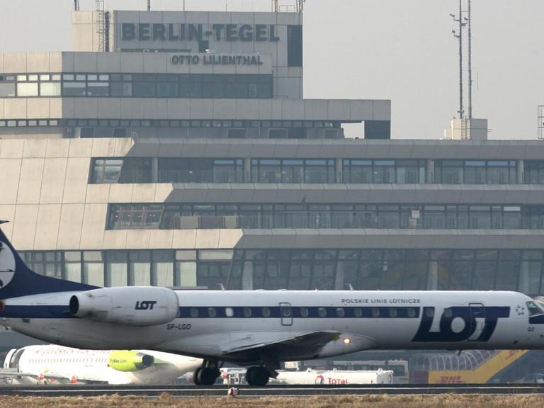 Ein Verkehrsflugzeug der polnischen Fluggesellschaft Lot steht auf dem Flughafen Berlin Tegel. Im Hintergrund sieht man den Tower und das Flughafengebäude.