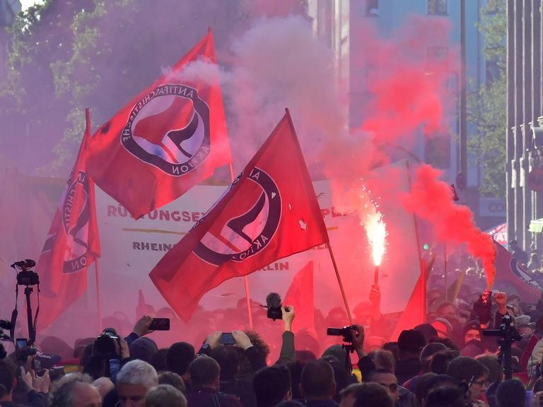 Viele Menschen stehen während einer Kundgebung am 1. Mai 2018 in Berlin in einer Straße. Es werden mehrere Fahnen mit dem Logo der Antifa hochgehalten.
