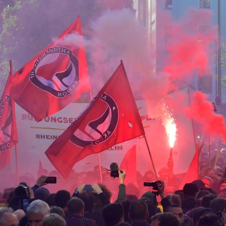Viele Menschen stehen während einer Kundgebung am 1. Mai 2018 in Berlin in einer Straße. Es werden mehrere Fahnen mit dem Logo der Antifa hochgehalten. 
