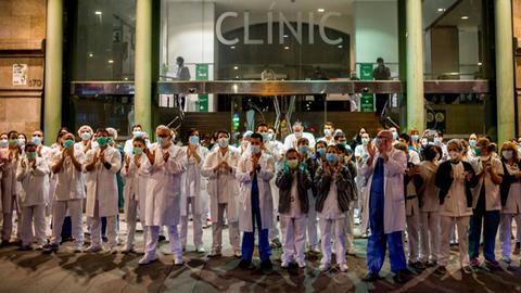 Klinikmitarbeiter in Kitteln und mit Mundschutz stehen vor dem Krankenhaus auf der Straße und applaudieren.