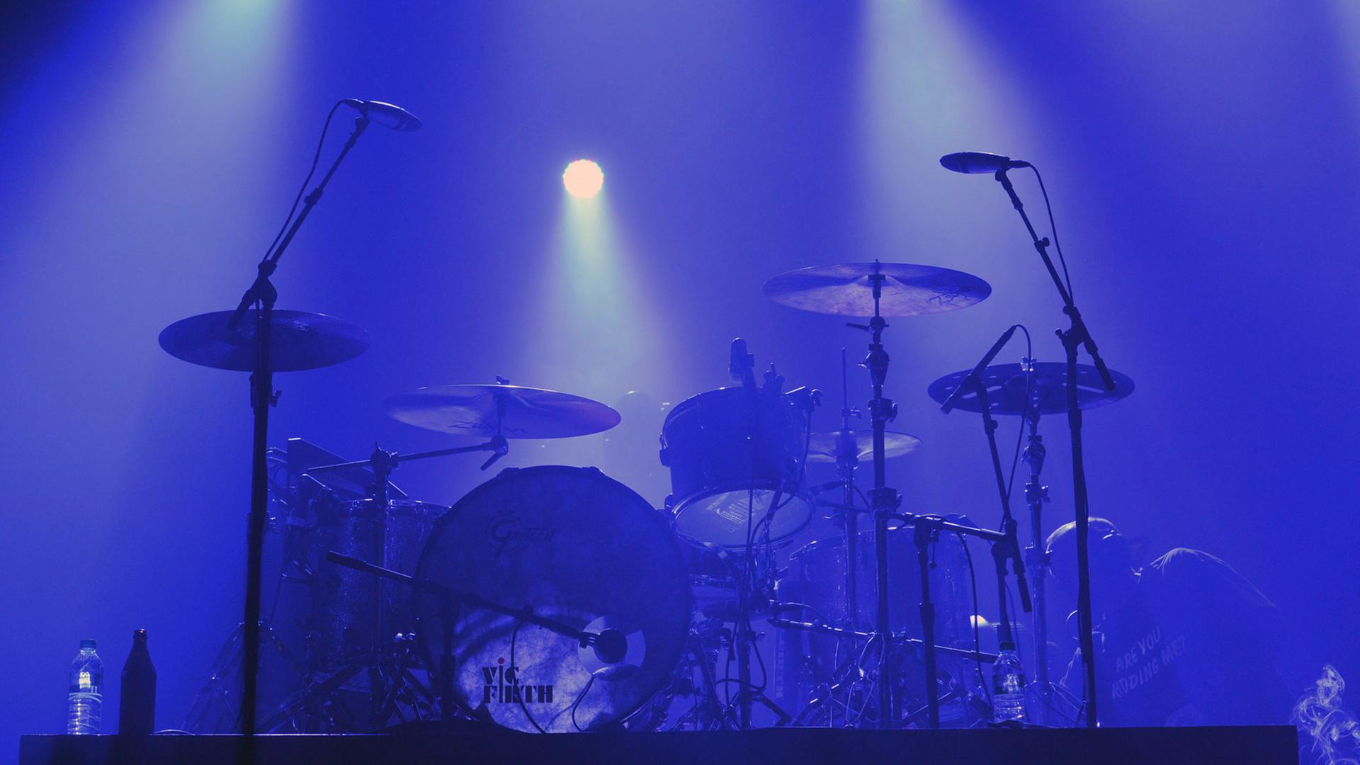 Eine in blaues Licht getauchte Bühne mit einem Schlagzeug, vor dem zwei Mikrofone stehen.
