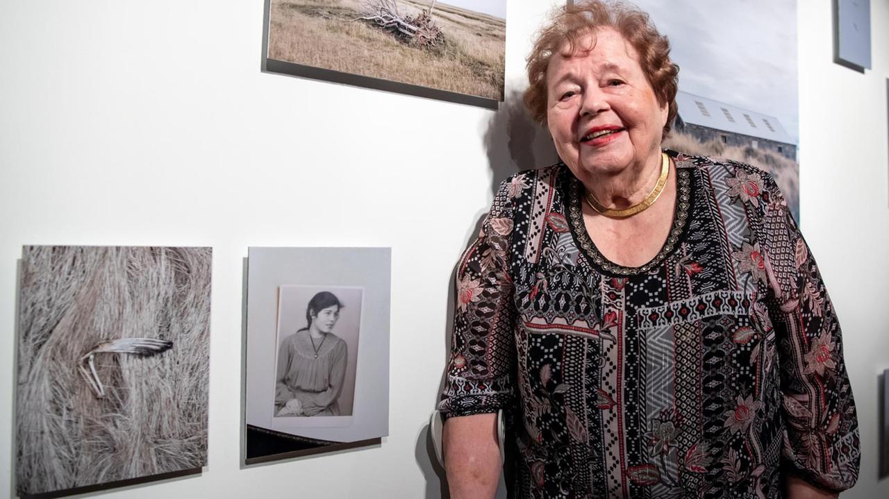 Eva Maria Jost-Magnusson steht in der Fotoausstellung über die 1949 übergesiedelten Deutschen neben einem Foto, das sie in jungen Jahren zeigt. 