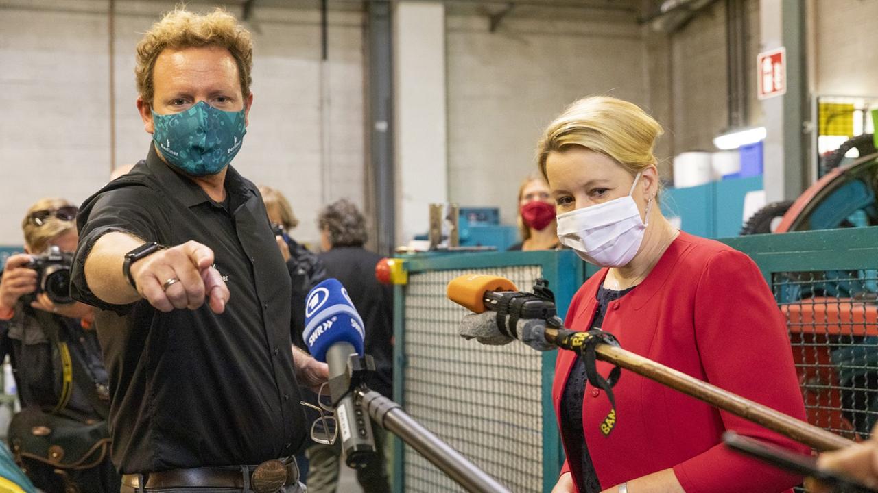 Mehrere Personen stehen in einer Werkshalle, und ein Mann erklärt etwas den Zuhörenden. Mehrere Personen stehen in einer Werkshalle, und ein Mann erklärt etwas den Zuhörenden.