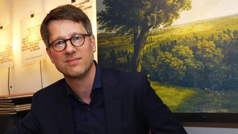 Der Lyriker Jan Wagner sitzt an einem Tisch mit Büchern und blickt freundlich in die Kamera. Der Lyriker Jan Wagner sitzt an einem Tisch mit Büchern und blickt freundlich in die Kamera.