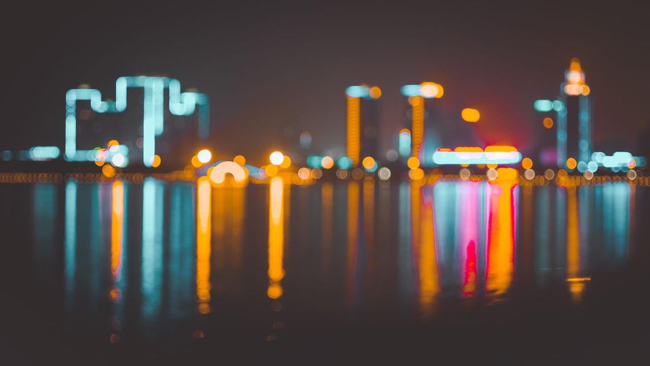 Eine bunt leuchtende Skyline spiegelt sich im Wasser. Eine bunt leuchtende Skyline spiegelt sich im Wasser.