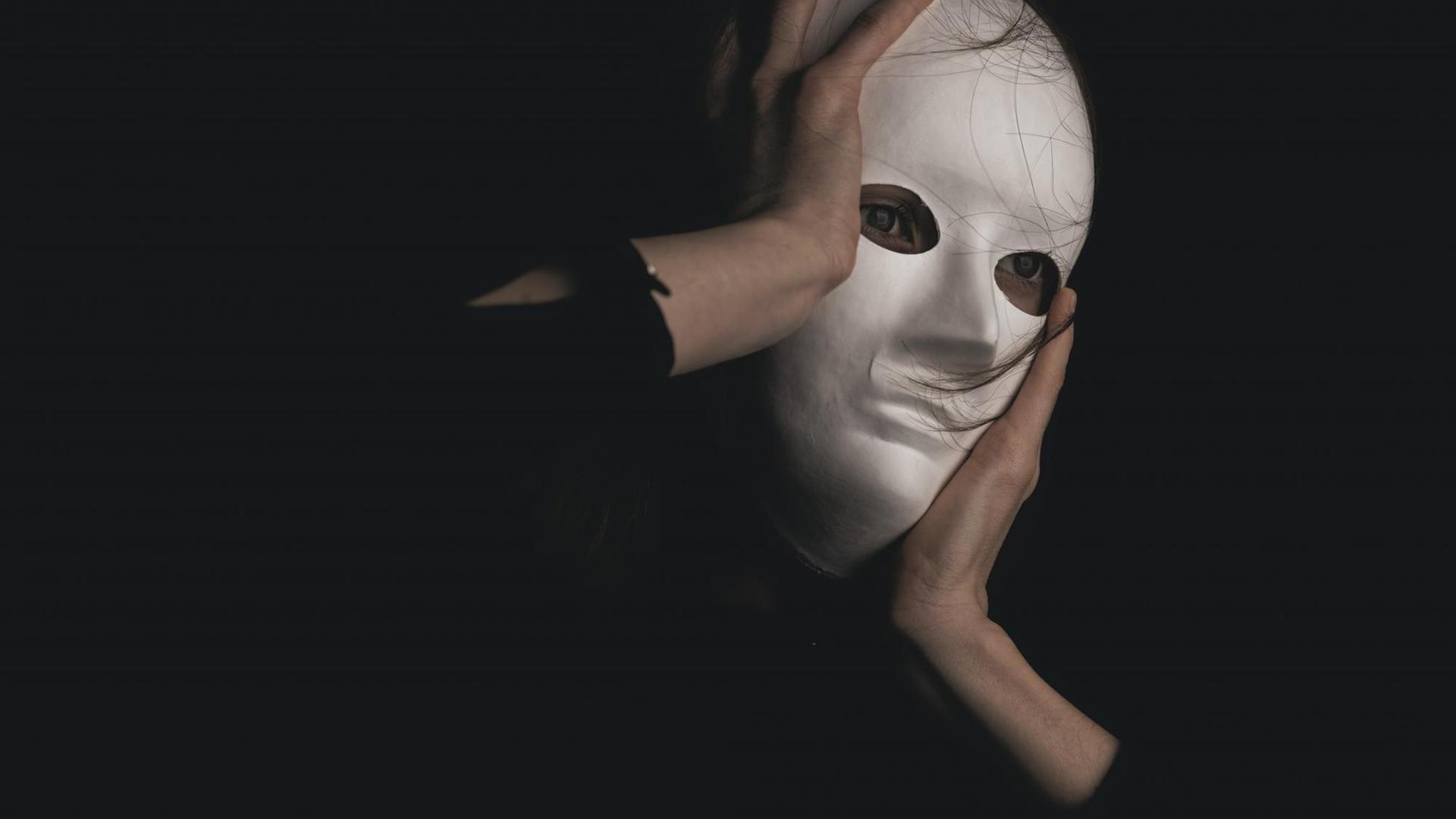 Ein Gesicht vor schwarzem Hintergrund, versteckt hinter einer Maske. Ein Gesicht vor schwarzem Hintergrund, versteckt hinter einer Maske.