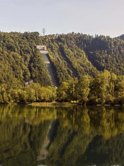Ansicht des Walchensee-Kraftwerks direkt am See zwischen bewaldeten Hügeln gelegen.