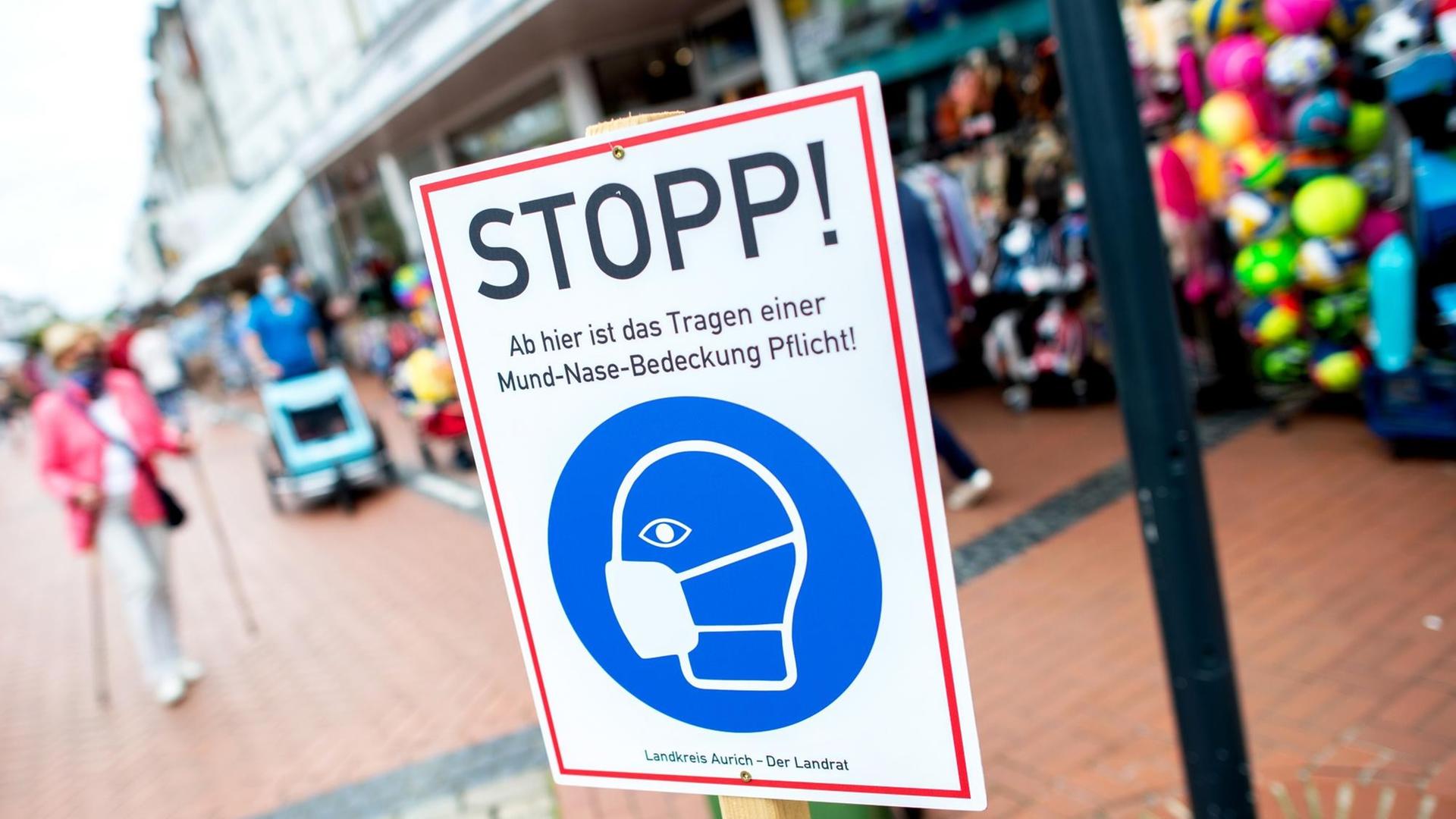 Ein Schild mit der Aufschrift "Stopp! Ab hier ist das Tragen einer Mund-Nasen-Bedeckung Pflicht!" steht in einer Fußgängerzone. Ein Schild mit der Aufschrift "Stopp! Ab hier ist das Tragen einer Mund-Nasen-Bedeckung Pflicht!" steht in einer Fußgängerzone.