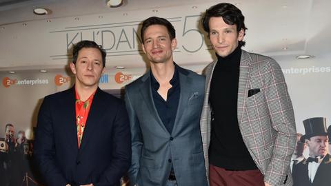 Die Schauspieler Trystan Pütter (l.), August Wittgenstein und Sabin Tambrea zur Premiere der ZDF-Serie "Ku'damm 59" im März 2018. Drei junge Männer im Anzug stehen vor einem Filmplakat.
