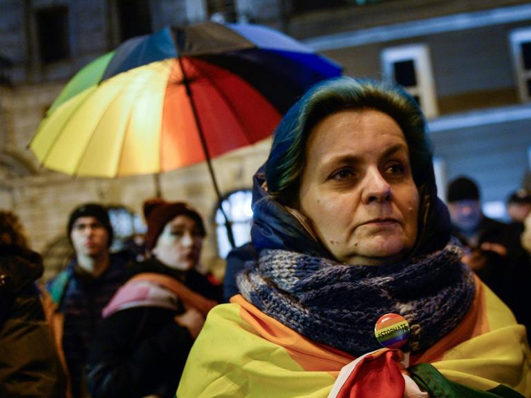Ein Frau in Warschau hat eine Regenbogenflagge um sich gewickelt. Im Hintergrund weitere Demonstranten. Sie demonstrieren gegen LGBT-freie Zonen in Polen.