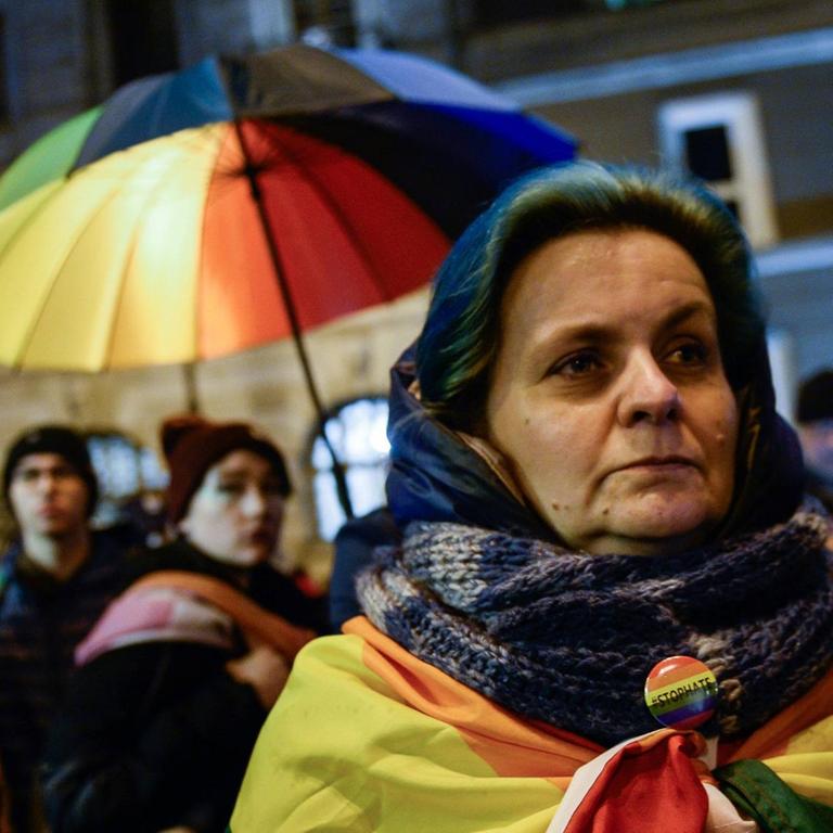 Ein Frau in Warschau hat eine Regenbogenflagge um sich gewickelt. Im Hintergrund weitere Demonstranten. Sie demonstrieren gegen LGBT-freie Zonen in Polen.