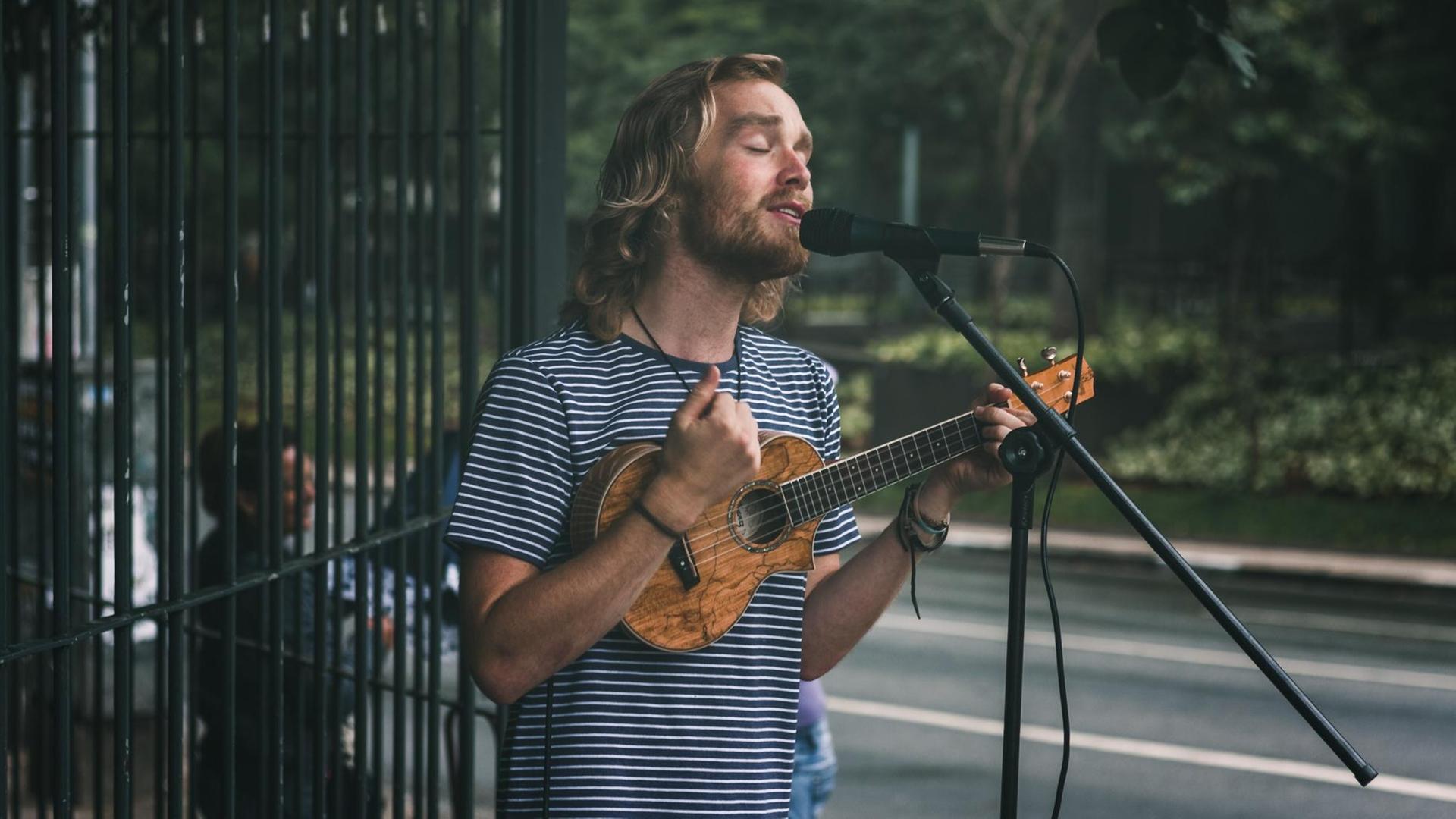 Ein junger Mann spielt auf der Straße Ukulele und singt. Ein junger Mann spielt auf der Straße Ukulele und singt.