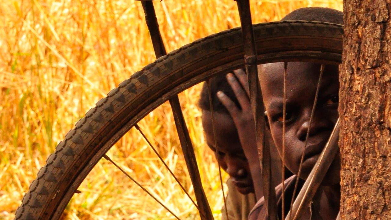 Ein Kind der Familie Ocan in Norduganda blickt durch die Speichen eines Rades.