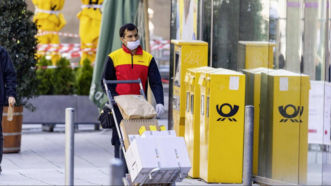 Ein DHL-Mitarbeiter mit Mund-Nase-Schutz liefert in Stuttgart Pakete aus. Ein DHL-Mitarbeiter mit Mund-Nase-Schutz liefert in Stuttgart Pakete aus.