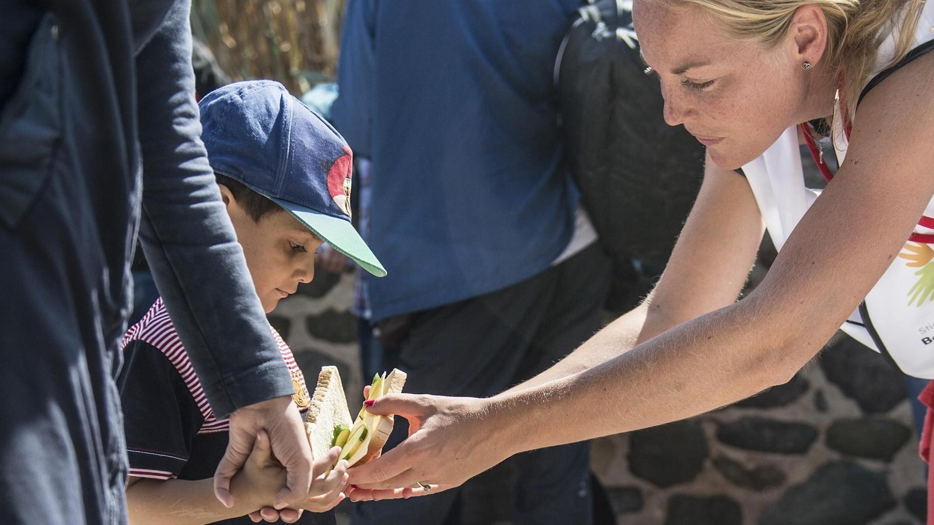 Eine Helferin auf Lesbos reicht einem geflüchteten Jungen Essen. Eine Helferin auf Lesbos reicht einem geflüchteten Jungen Essen.