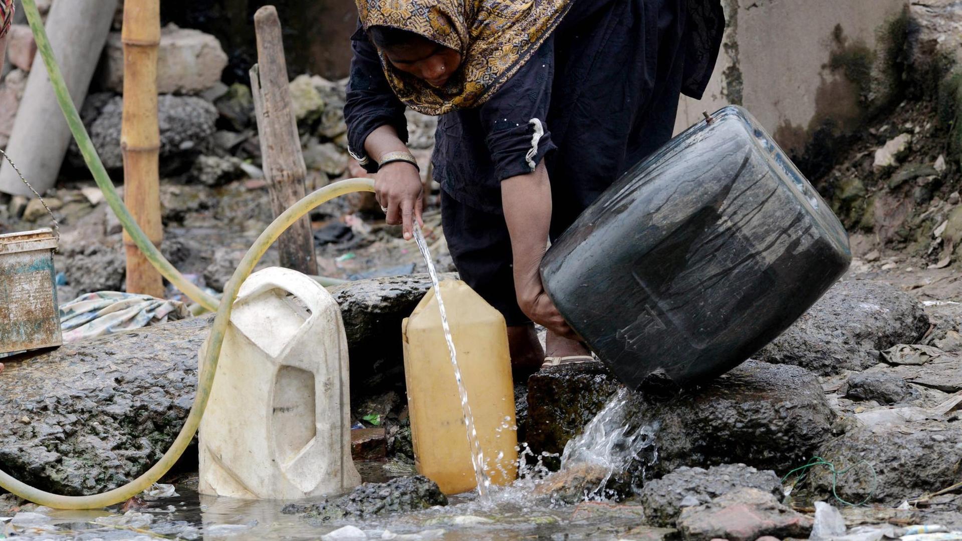 Eine pakistanische Frau füllt Gefäße mit Trinkwasser an einem Brunnen. Eine pakistanische Frau füllt Gefäße mit Trinkwasser an einem Brunnen.