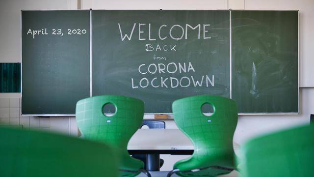 Ein leeres Klassenzimmer mit grünen Stühlen und einer Tafel, auf der steht: "Welcome Back From Corona Lockdown"-