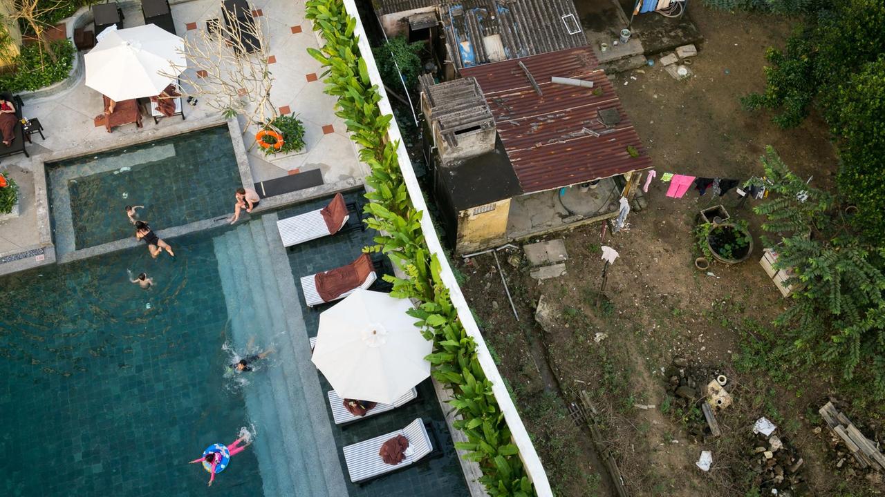 Reich und Arm in Vietnam dicht beieinander: Eine moderne Hotelanlage mit Schwimmbecken und grünen Pflanzen in Hoi An ist nur durch eine weiße Mauer getrennt von einem verrosteten Haus mit rostigem Wellblechdach. Reich und Arm in Vietnam dicht beieinander: Eine moderne Hotelanlage mit Schwimmbecken und grünen Pflanzen in Hoi An ist nur durch eine weiße Mauer getrennt von einem verrosteten Haus mit rostigem Wellblechdach.