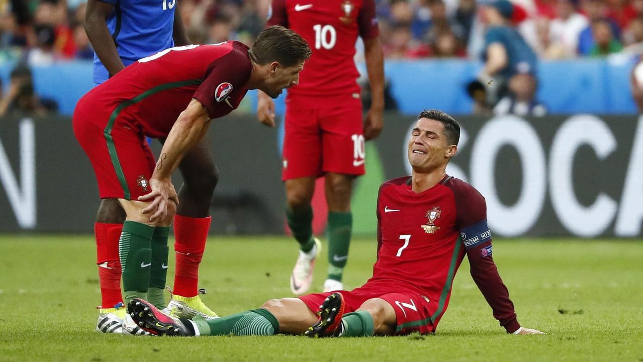 Cristiano Ronaldo sitzt auf dem Rasen und verzieht das Gesicht.