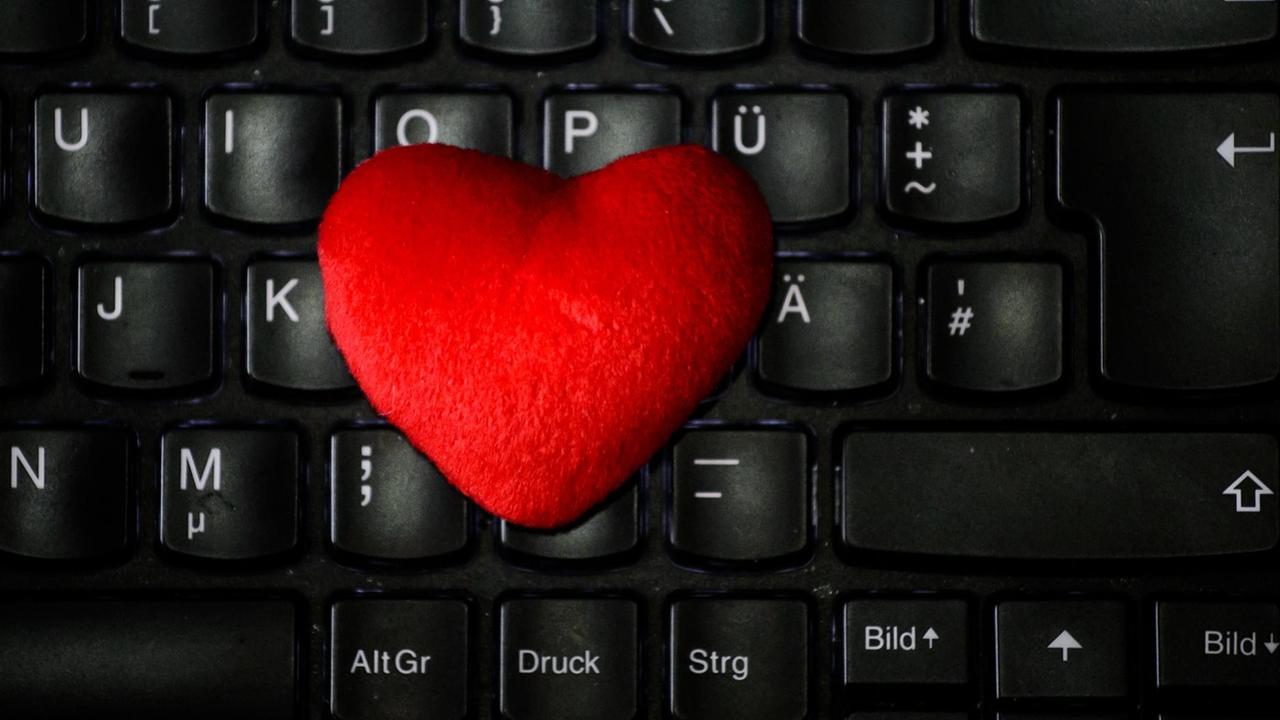 Ein rotes Herz aus Stoff liegt auf der Tastatur eines Notebooks.