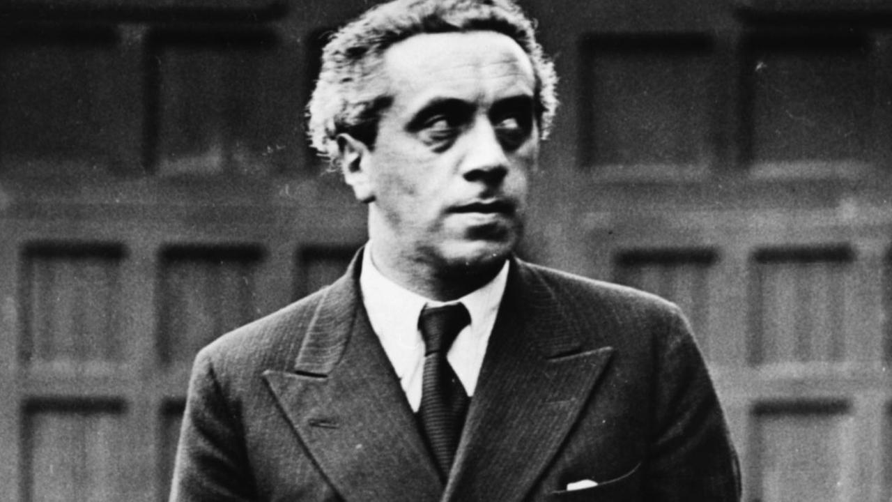 Ernst Toller trägt einen Anzug, hat eine Hand in der Hostentasche und blickt ernst ins Off. Ernst Toller trägt einen Anzug, hat eine Hand in der Hostentasche und blickt ernst ins Off.
