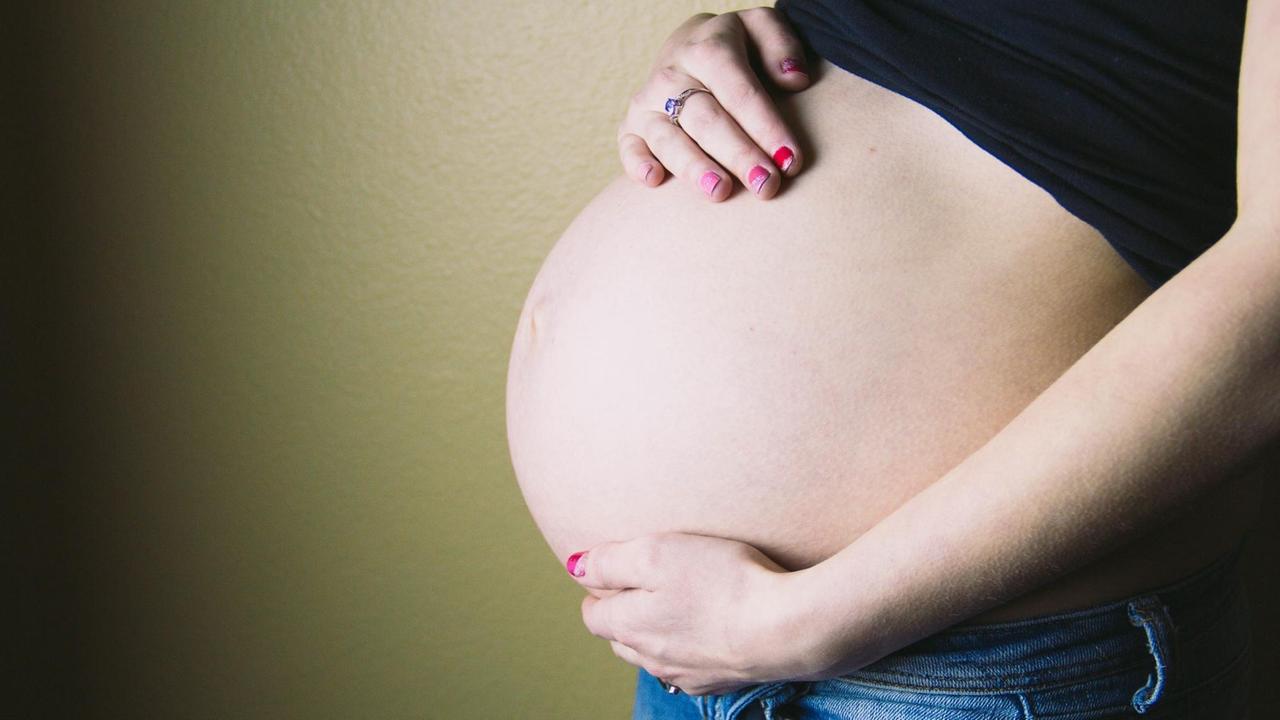 Eine junge Mutter mit pink lackierten Fingernägeln hält sich ihren Schwangerschaftsbauch.