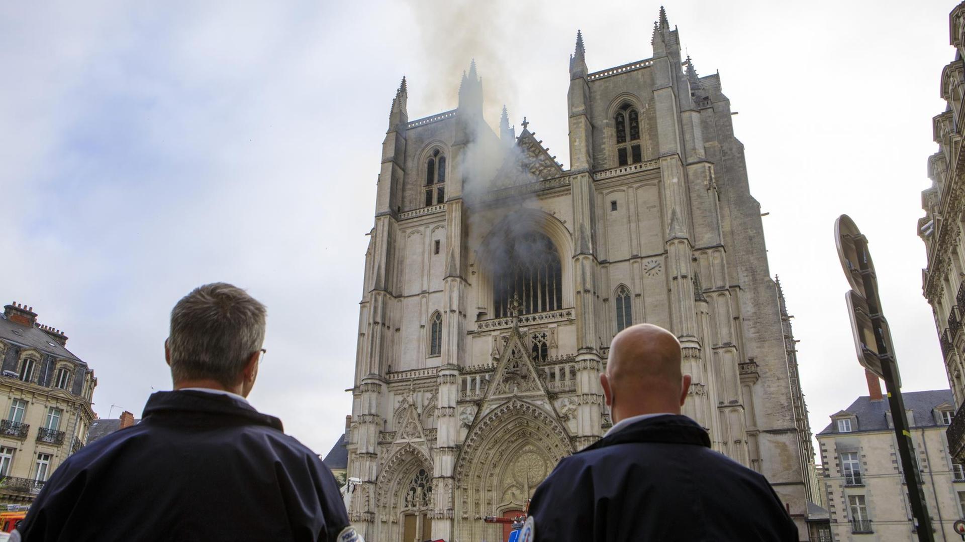 Polizisten beobachten, wie Rauch aus einem Fenster der Kathedrale Saint-Pierre-et-Saint-Paul im französischen Nantes steigt.