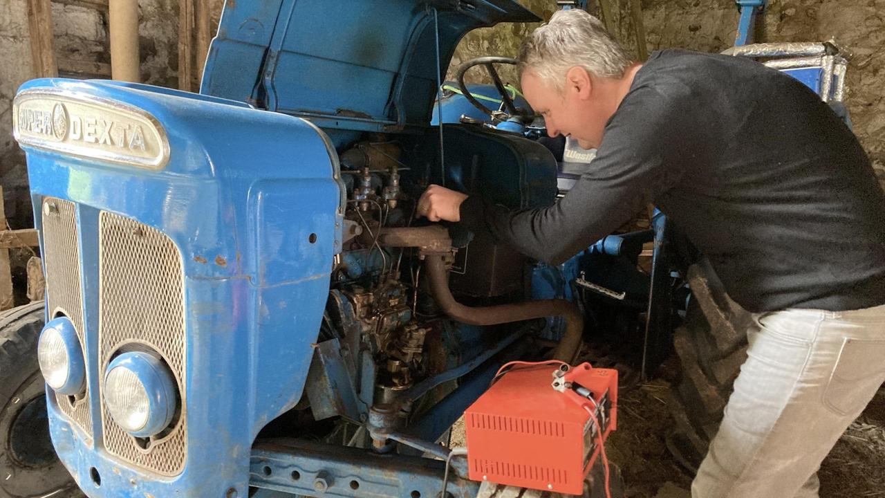 Ein Mann schraubt an einem historischen blauen Trecker. Ein Mann schraubt an einem historischen blauen Trecker.