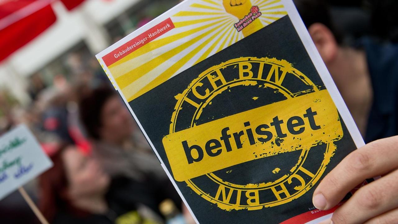 Ein Mitarbeiter des Gebäudereiniger-Handwerks hält am 01.05.2014 in Nürnberg (Bayern) auf einer Kundgebung vom Deutschen Gewerkschaftsbund (DGB) einen Protest-Flyer gegen befristete Arbeitsverhältnisse in seiner Branche in der Hand. Ein Mitarbeiter des Gebäudereiniger-Handwerks hält am 01.05.2014 in Nürnberg (Bayern) auf einer Kundgebung vom Deutschen Gewerkschaftsbund (DGB) einen Protest-Flyer gegen befristete Arbeitsverhältnisse in seiner Branche in der Hand.