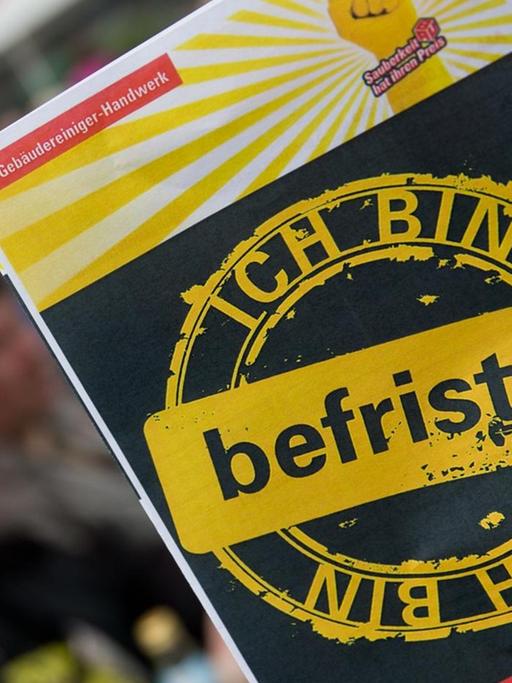 Ein Mitarbeiter des Gebäudereiniger-Handwerks hält am 01.05.2014 in Nürnberg (Bayern) auf einer Kundgebung vom Deutschen Gewerkschaftsbund (DGB) einen Protest-Flyer gegen befristete Arbeitsverhältnisse in seiner Branche in der Hand.