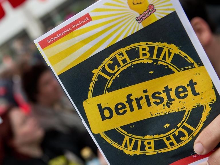 Ein Mitarbeiter des Gebäudereiniger-Handwerks hält am 01.05.2014 in Nürnberg (Bayern) auf einer Kundgebung vom Deutschen Gewerkschaftsbund (DGB) einen Protest-Flyer gegen befristete Arbeitsverhältnisse in seiner Branche in der Hand.