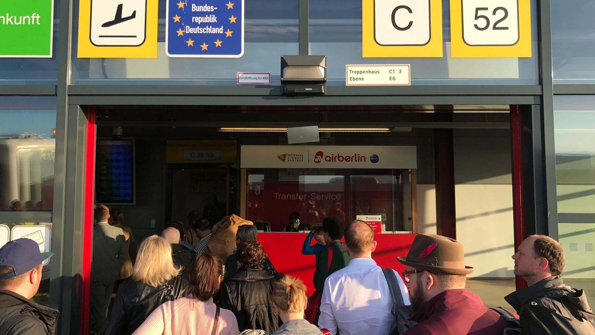 Die geöffnete Tür des Terminals C am Flughafen Berlin-Tegel, davor eine Gruppe Fluggäste in Rückenansicht.