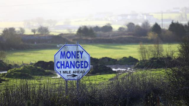 Ein Straßenschild mit der Aufschrift "Money Changed" (Geld wechseln) steht in einer Hecke an der Grenze zwischen Nordirland und der Republik Irland.