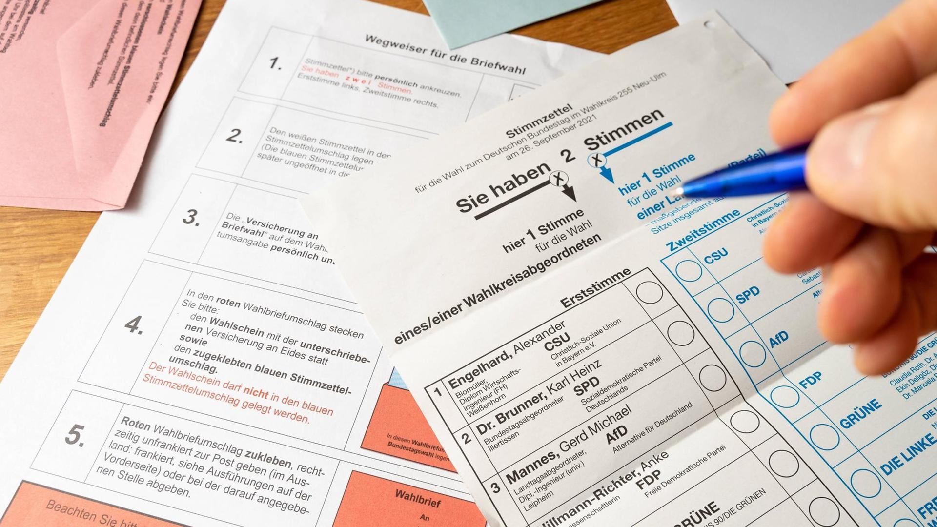 Großaufnahme des Stimmzettels zur Bundestagswahl 2021 mit Möglichkeit zum Ankreuzen von Erst- und Zweitstimme. Zu sehen sind außerdem eine Hand, die einen Kugelschreiber hält, und einige Zettel mit Erläuterungen zur Briefwahl. Großaufnahme des Stimmzettels zur Bundestagswahl 2021 mit Möglichkeit zum Ankreuzen von Erst- und Zweitstimme. Zu sehen sind außerdem eine Hand, die einen Kugelschreiber hält, und einige Zettel mit Erläuterungen zur Briefwahl.