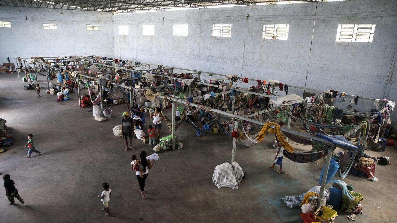 In einer Lagerhalle haben sich die Flüchtlinge mit Hängematten, die an Metallposten gebunden sind, notdürftig eingerichtet. 