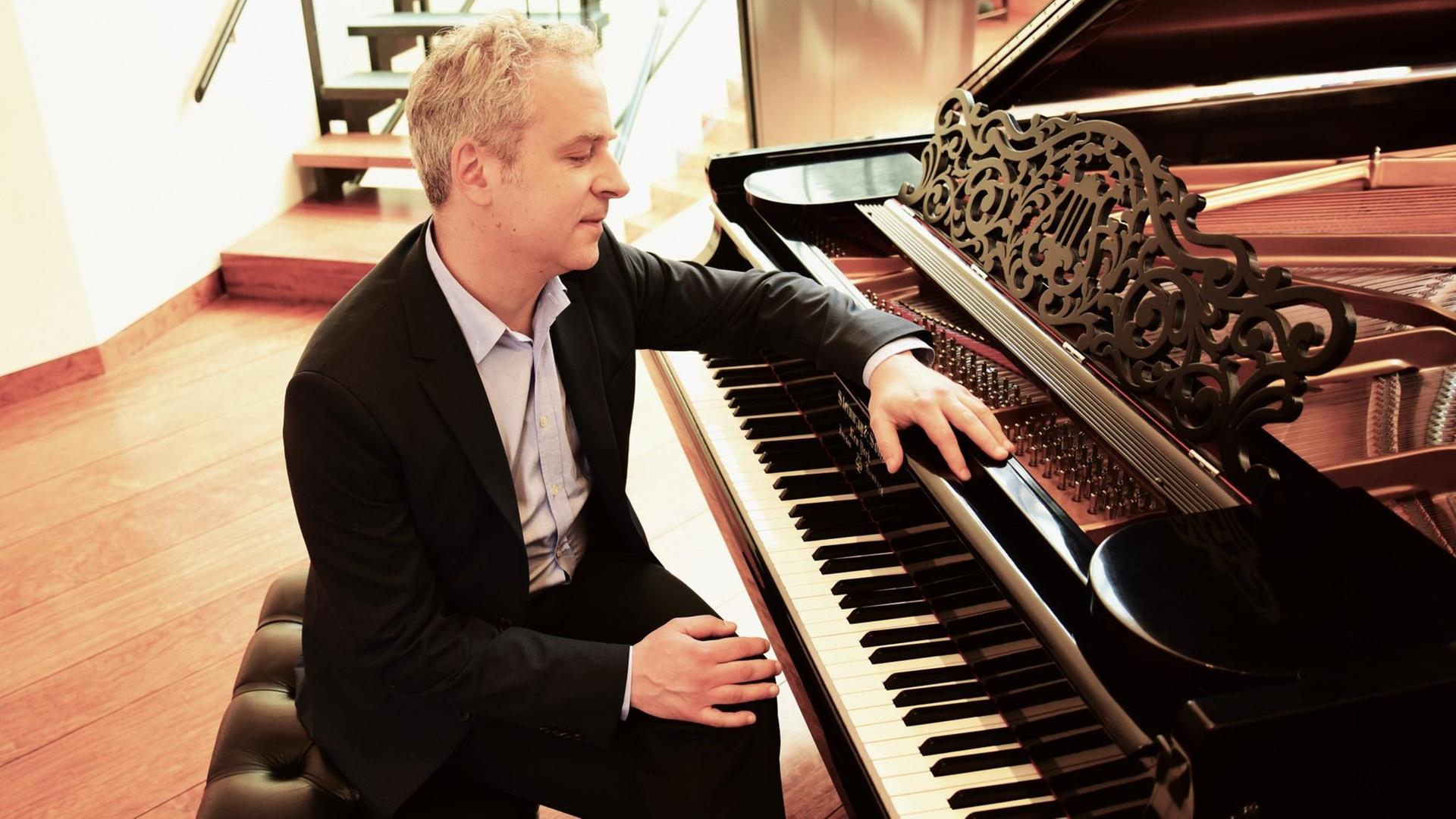 Ein Pianist sitzt mit überschlagenen Beinen vor einem Flügel, lehnt sich mit einem Arm locker auf das Instrument. Ein Pianist sitzt mit überschlagenen Beinen vor einem Flügel, lehnt sich mit einem Arm locker auf das Instrument.